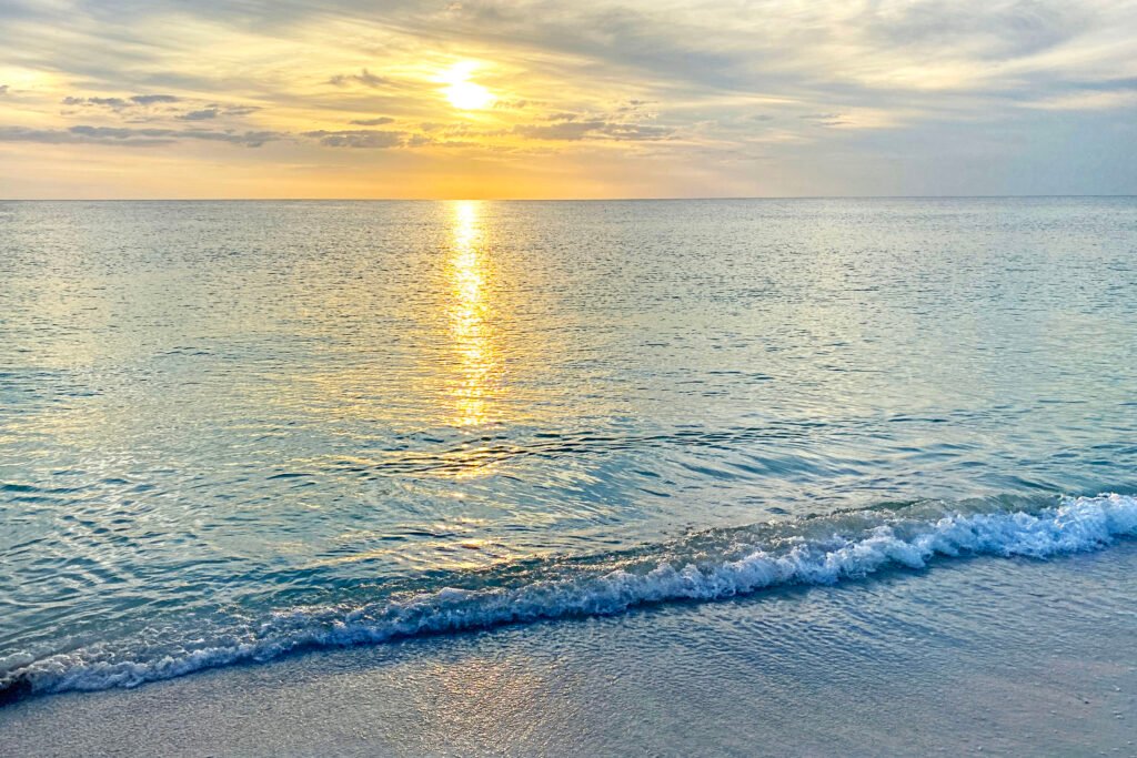 An image on the beach of the sun setting over the gulf waters. 