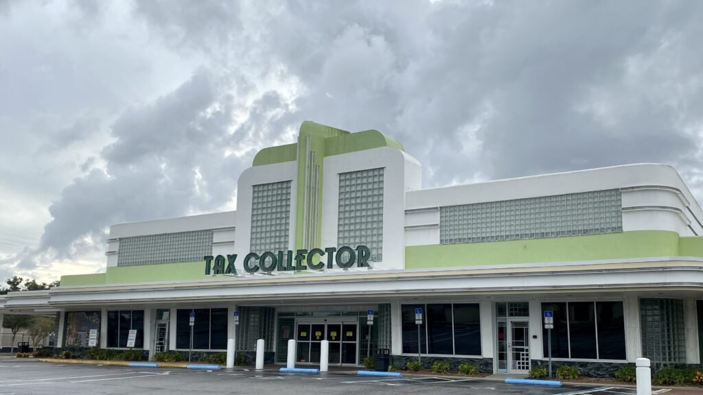 An image of a Tax Collector building in Lakeland, Florida. The tax collector building is built out of an old movie therater, complete with neon sign and bright green paint. 